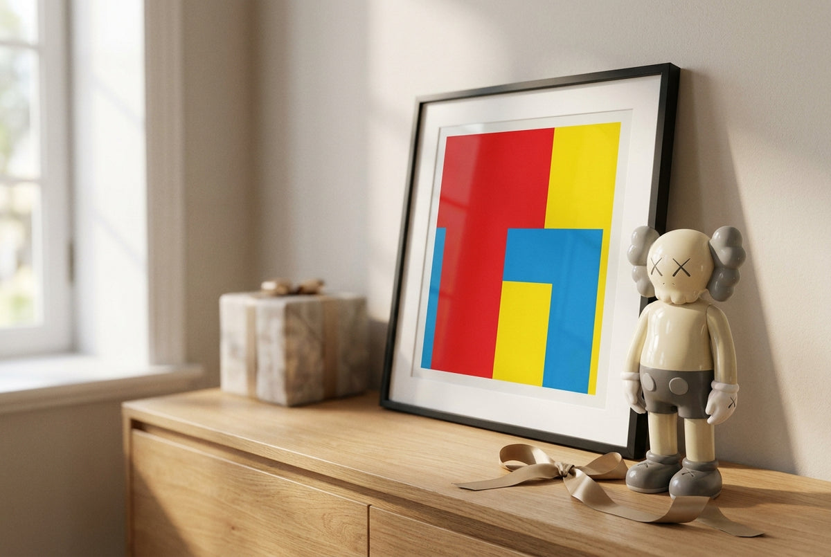 A framed pop-art print in bold red, yellow and blue beside a designer art figure, styled as gifts on a console table