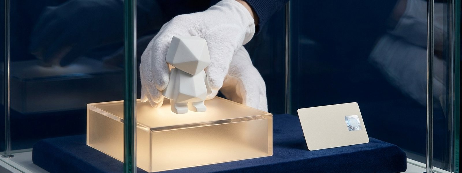 White-gloved hands placing a collectible art figure on a lit display riser beside an authentication certificate
