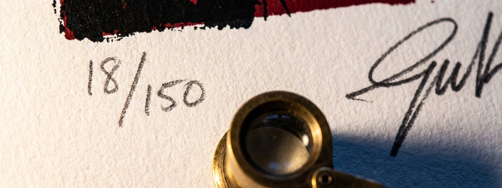 Macro of a screen print margin showing a graphite pencil edition number 18 of 150 and a handwritten signature beside a brass loupe