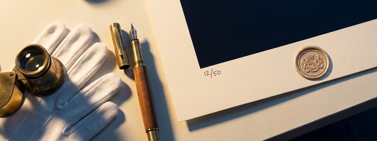 Flat-lay of a hand-numbered art print with an embossed gold wax authentication seal, fountain pen, cotton gloves and a brass loupe