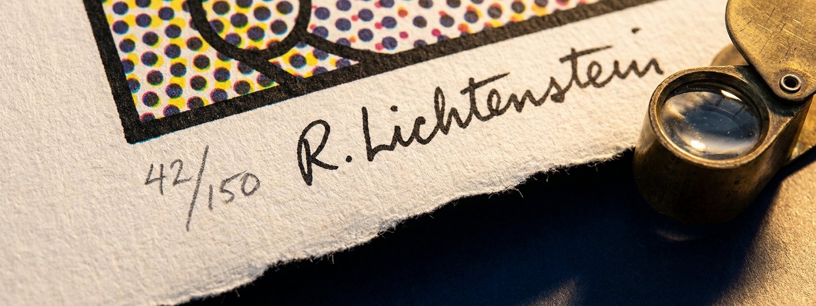 Macro of a pop-art print's lower margin showing a pencil edition fraction and handwritten signature beside a brass loupe