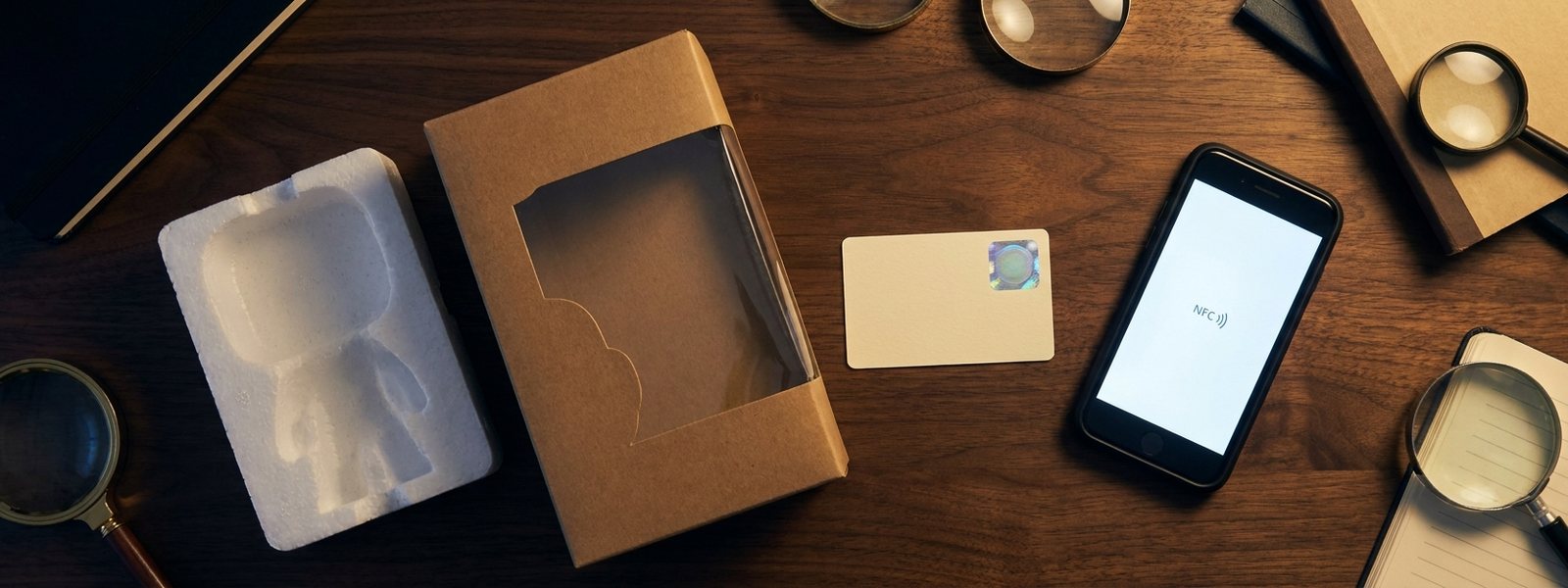 Collectible box, foam insert, authentication card with hologram and an NFC verification screen on a walnut table