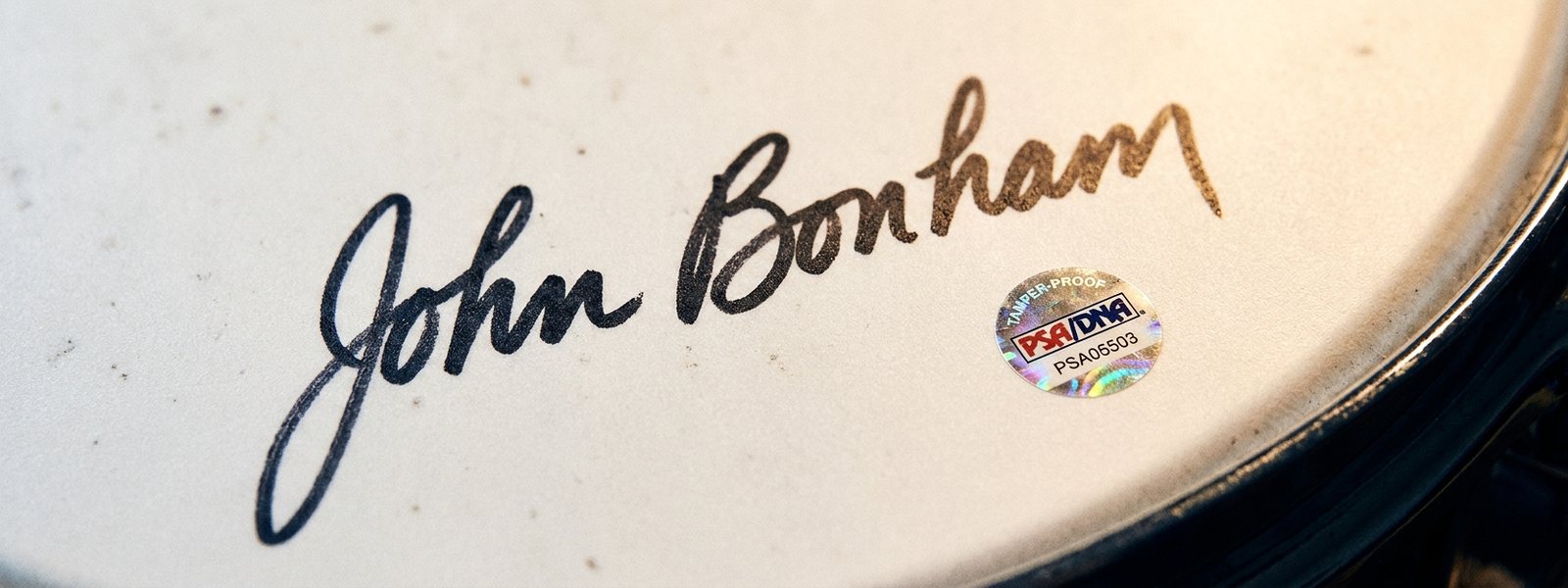 Extreme macro of a signed white drumhead showing a black marker signature and a round tamper-proof authentication hologram sticker