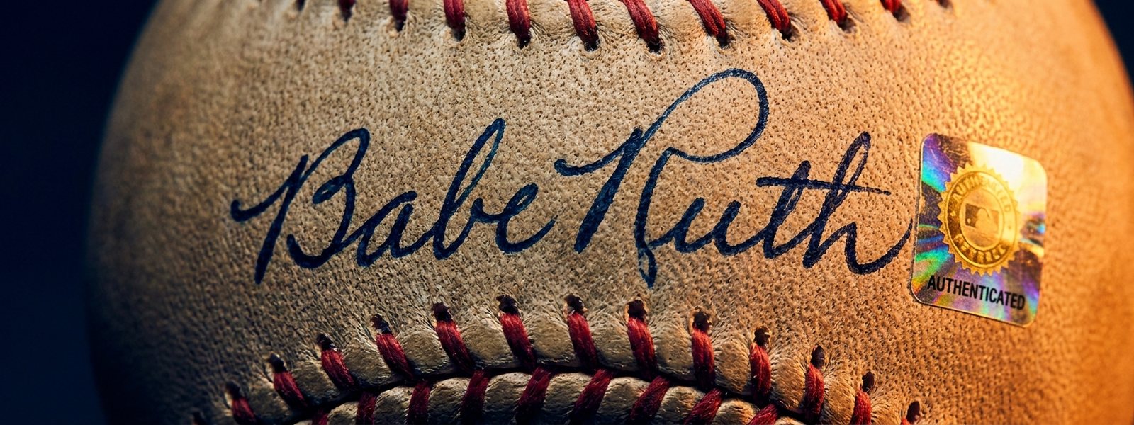 Extreme macro of a flowing blue-ink signature across a ball's leather seams beside a tamper-proof authentication hologram sticker